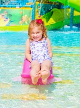 Smiling cheerful baby girl enjoying water attractions, warm sunny day, swimming in poolside, carefree childhood, summer vacation
