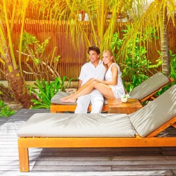 Cute happy couple having fun outdoors, sitting on sunbed on luxury tropical resort, sunny day, romantic summer vacation, love concept