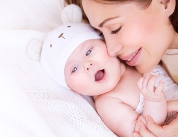 Closeup portrait of beautiful gentle mother playing with cute little baby lying down on the bed, closed eyes of pleasure, loving young family, happy motherhood concept