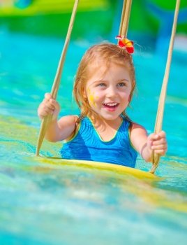 Closeup on cheerful baby girl with face paint swinging on water attractions, having fun in poolside, summer vacation, happy childhood concept