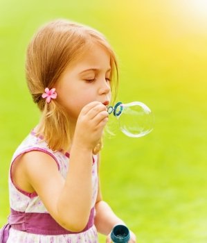 Closeup portrait of cute baby girl blowing soap bubbles in spring park, having fun outdoors, happy childhood concept