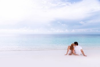 Rear view of loving couple relaxing on the beach, kissing outdoors, boyfriend with girlfriend enjoying summer holidays on luxury Maldives resort, love and romance concept
