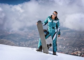 Sportive woman standing on the top of mountain with snowboard in hands, active wintertime holidays, extreme lifestyle concept
