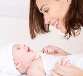 Closeup portrait of beautiful cheerful mother playing with cute little baby lying down on the bed, loving young family, happy motherhood concept