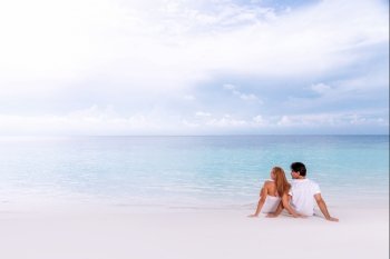 Rear view of loving couple relaxing on the beach, boyfriend with girlfriend enjoying summer holidays on luxury Maldives resort, love and romance concept

