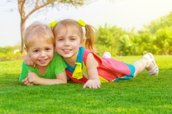 Picture of cute little girl with pretty boy lying down on green grass in park, cheerful children resting on the field on backyard, brother and sister having fun outdoors in springtime, happy childhood