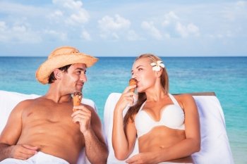 Happy couple relaxing on the beach resort, sitting on sunbed, eating tasty ice cream and looking on each other, romantic honeymoon