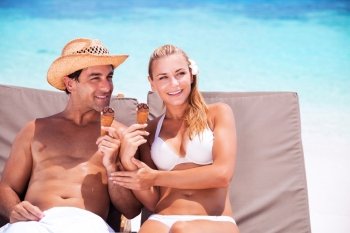 Happy couple on the beach sitting on sunbed and eating ice cream, with interest looking in side, enjoying summer vacation
