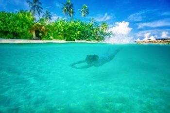 Young active woman diving near Maldives island, enjoying marine life, swimming with pleasure in the Indian sea, summer vacation concept