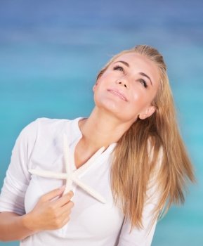 Portrait of pretty girl on the beach in sunny day with starfish in hand and dreamy looking up in the sky, enjoying summer vacation on tropical resort on Maldives