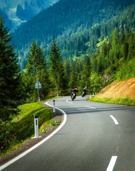 Group of motorcyclists in Alpine mountains, moto racers on curve mountainous road, touring along Europe, travel and tourism concept