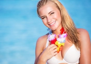 Portrait of cute blond female wearing beautiful Hawaiian leis, having fun on the beach, tropical party with traditional flowers garland on neck
