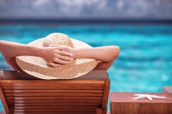 Luxury female tanning on the beach, wearing big stylish hat, enjoying beautiful seascape, summer fashion, travel and tourism concept