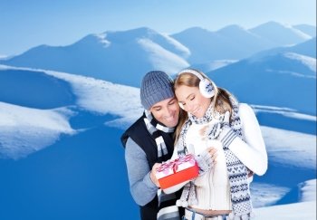 Happy couple with gift, people outdoor at winter snow mountains, young man giving present to beautiful woman, Christmas vacation holidays, love concept
