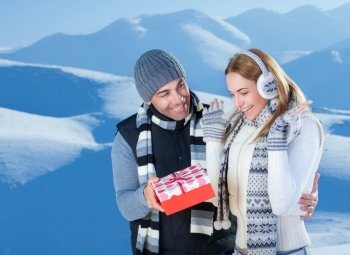Handsome cheerful man giving to her precious girlfriend red gift box, celebrating Christmas holidays in the beautiful snowy mountains

