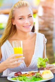 Closeup portrait of beautiful young happy female having lunch outdoors, drink refreshing orange juice and eating green salad, healthy eating concept