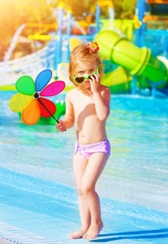 Cute little girl having fun in aquapark, holding in hand big colorful flower toy, water attractions, enjoying summer holidays, happy childhood concept