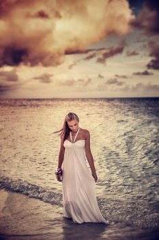 Grunge style photo of beautiful young woman on the beach in overcast weather, dramatic cloudscape, sadness and solitude concept
