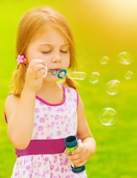 Closeup portrait of cute baby girl blowing soap bubbles outdoors, playing game on spring garden, sunny day, happy childhood concept