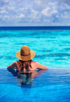 Rear view of young lady relaxing in the pool and enjoying view of beautiful seascape, refreshing in cool transparent water, summer holidays concept