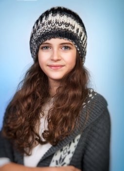 Portrait of cute teen girl wearing stylish knitted hat and sweater isolated on blue background, winter fashion for teenagers