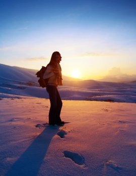 Woman traveler hiking in winter mountains, trekking in wintertime cold snowy weather, girl silhouette over natural colorful sky with bright sunset and beautiful landscape, freedom concept