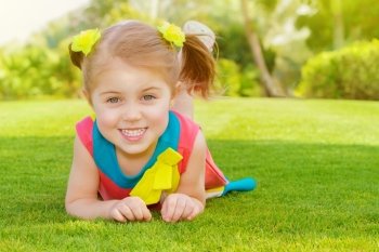 Picture of cute little girl lying down on green grass in park, cheerful child resting on the field on backyard, pretty kid having fun outdoors in springtime, spring nature, sunny day, happy childhood