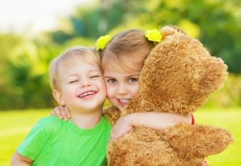 Photo two cute child hugging outdoors, brother and sister having fun on backyard in spring, nice little girl with adorable boy playing with big soft bear toy, best friends, happy childhood concept