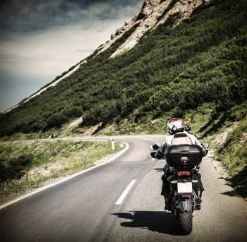Racer on mountainous highway, biker riding along Alpine mountains, travel to Europe, summer vacation, extreme sport