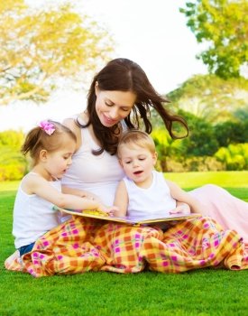 Picture of beautiful woman with daughter and son sitting down on green grass field and read fairytale, cheerful mother and two pretty kids enjoying book on backyard in spring, happy family concept