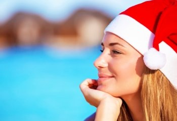 Portrait of pretty woman wearing red Santa hat and dreamy looking on side, Christmastime holidays on the beach on exotic island, luxury winter time vacation concept