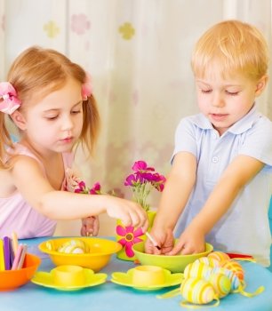 Two serious children paint Easter eggs at home, using colorful decoration, Christian holiday concept