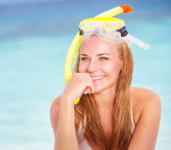 Portrait of beautiful blond girl wearing cute yellow diving mask sitting on the beach, active lifestyle, enjoying water sport, summer vacation concept
