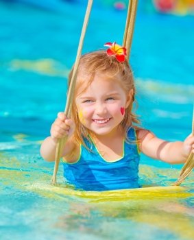 Cute happy girl enjoying summer holiday in the pool, having fun on water swing, red frangipani flower in hair, red heart print and yellow sun print on cheeks