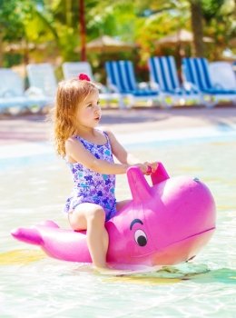 Cute little girl floating in aquapark, having fun in poolside in daycare, summer holidays, water attractions, happy childhood concept