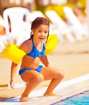 Cute little girl preparing to jump into water, having fun in the pool, luxury beach resort, summer time in daycare, holiday and vacation concept
