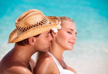 Portrait of handsome man kissing his nice young wife, closed eyes of pleasure, enjoying each other on the beach, summer vacation on exotic resort