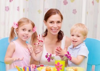 Happy young family playing with colorful paint at home, mother with two adorable children decorate Easter eggs