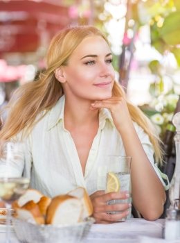 Portrait of cute blond female drink water with lemon in nice outdoor European cafe, healthy lifestyle, enjoying wonderful summer traveling to Italy