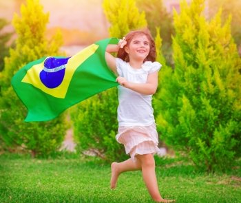 Happy little football fan, cute little girl running on the park with national Brazil flag waving on the wind, sportive childhood, football championship concept