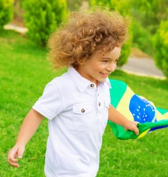 Portrait of cute little boy running with Brazil national flag, cheerful young football player, fan of Brazilian football team