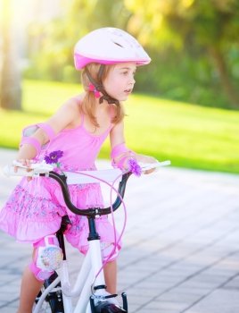 Cute little girl riding a bike in the park in bright sunny day, wearing nice pink dress, enjoying summer sport, happy childhood concept
