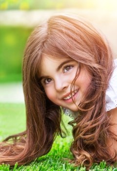 Closeup portrait of cute little girl lying down on fresh green grass field, having fun outdoors, relaxing in the park, happy childhood concept