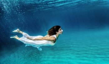 Happy girl swimming underwater, wearing stylish dress, luxury sea performance, active summer vacation, relaxation and enjoyment concept