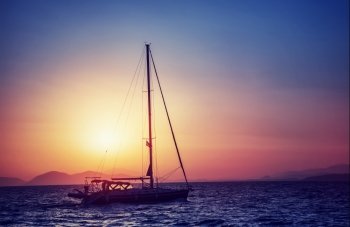 Silhouette of sailboat on sunset, water transport in bright yellow sun light, sea trip in the evening, traveling around Greek islands