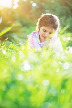 Dreamy photo of a nice little arabic girl on the fresh green grass field, cute child enjoying spring nature, with pleasure spending time outdoors