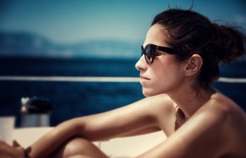 Closeup portrait of attractive female sitting on the yacht deck and enjoying warm sunny day, fashionable look, side view, sea cruise, traveling on luxury water transport
