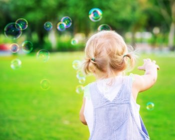 Little baby girl try to catch soap bubbles, having fun outdoors, playing games in the park, happy carefree childhood