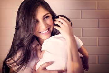 Closeup portrait of cheerful smiling mother with sleeping newborn daughter on her shoulder at home, happy young loving family, new life concept