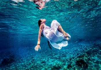 Gorgeous female dancing underwater, wearing long white fashion dress, summer activity, relaxation in blue transparent sea, enjoyment and refreshment concept